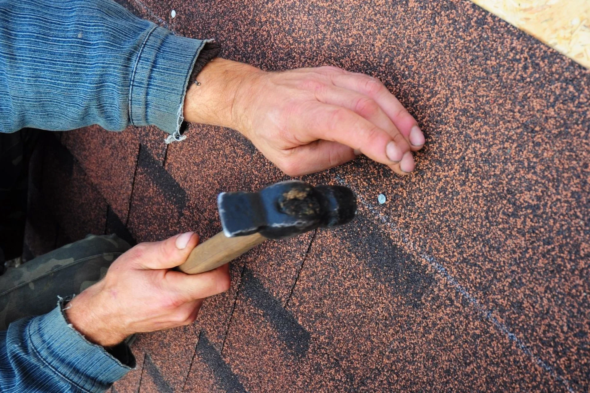 A person using a hammer to fix the shingles on a roof.